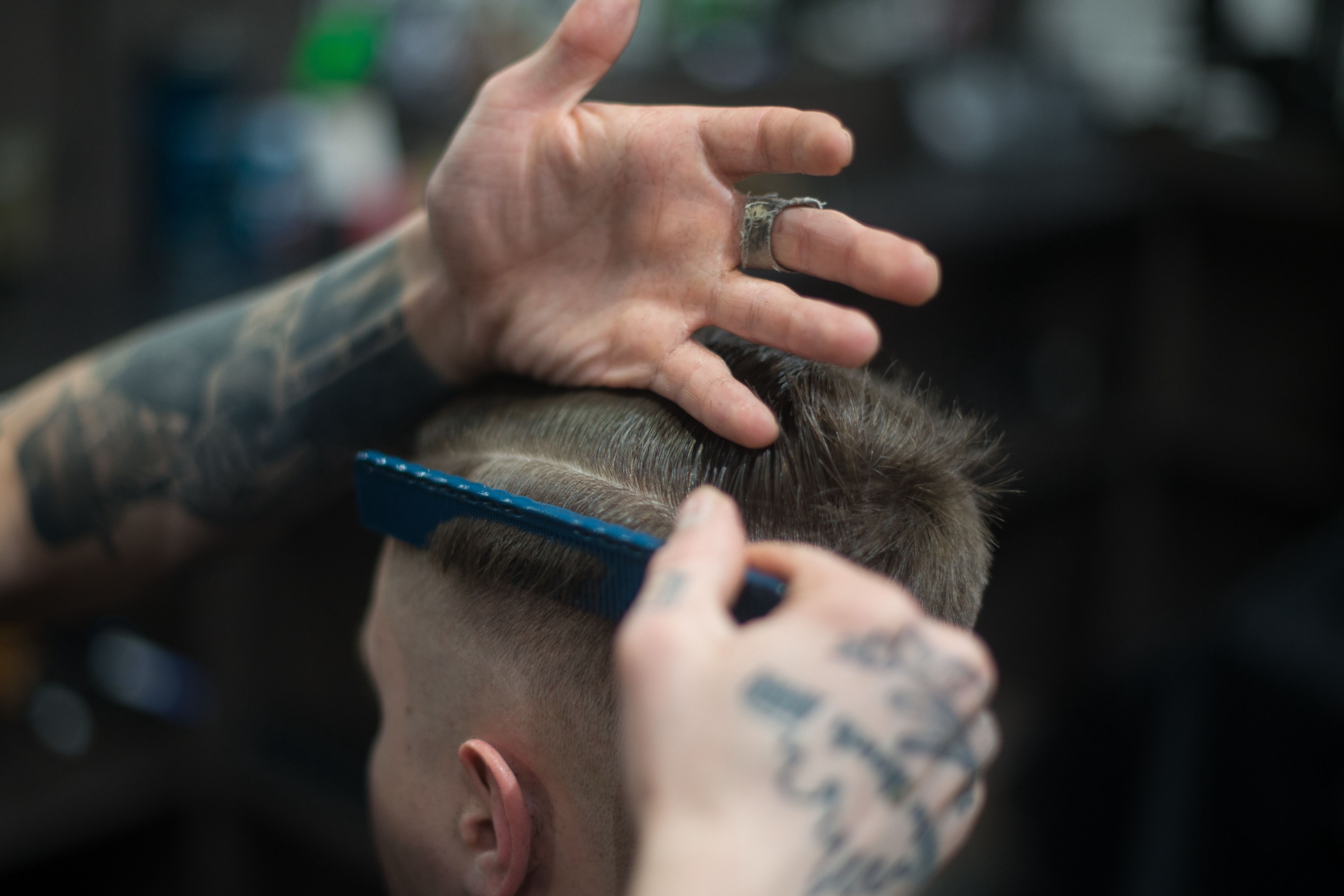A barber with tattoos doing a fade out.