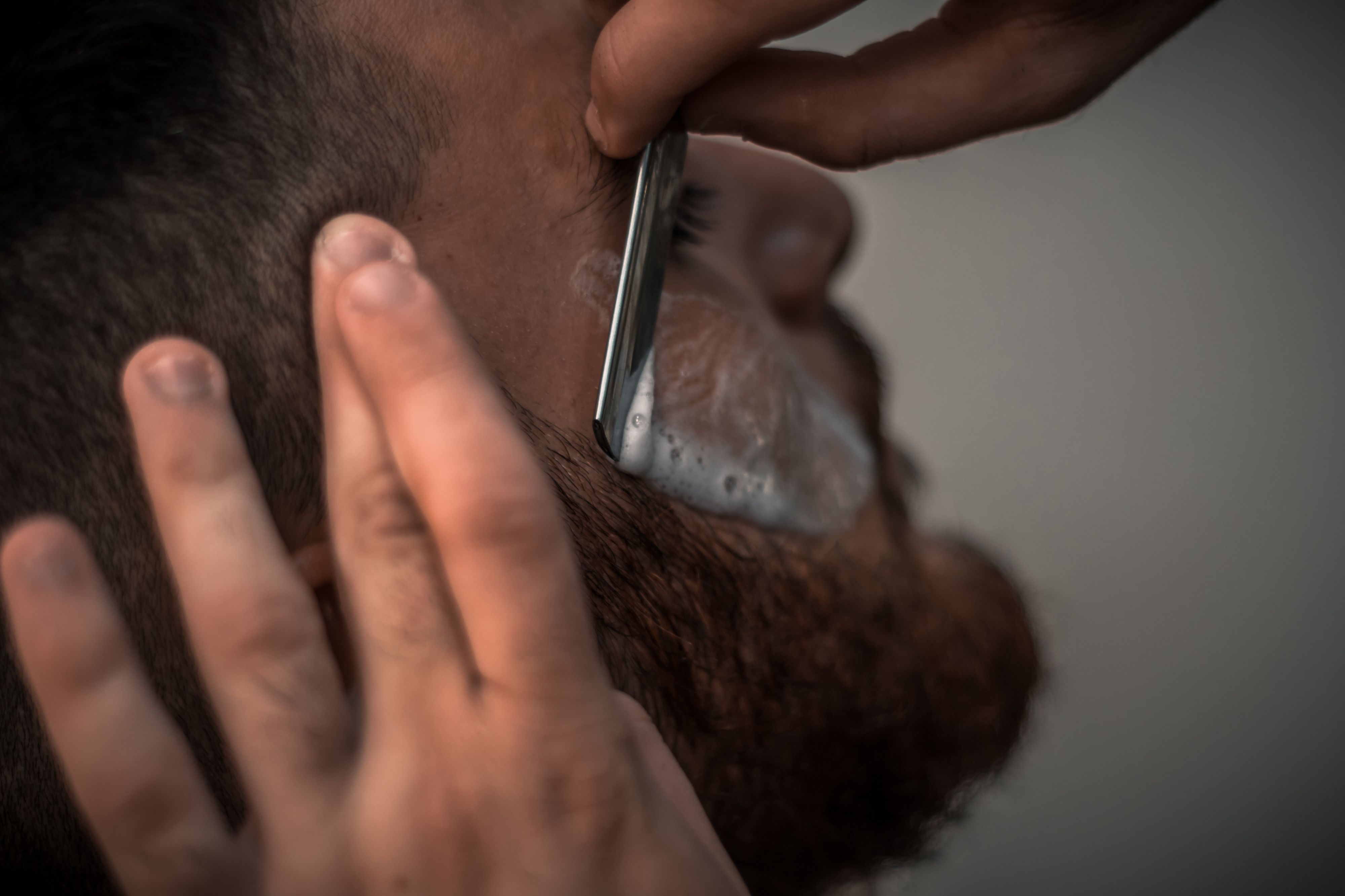 A barber shaving a beard using razor
