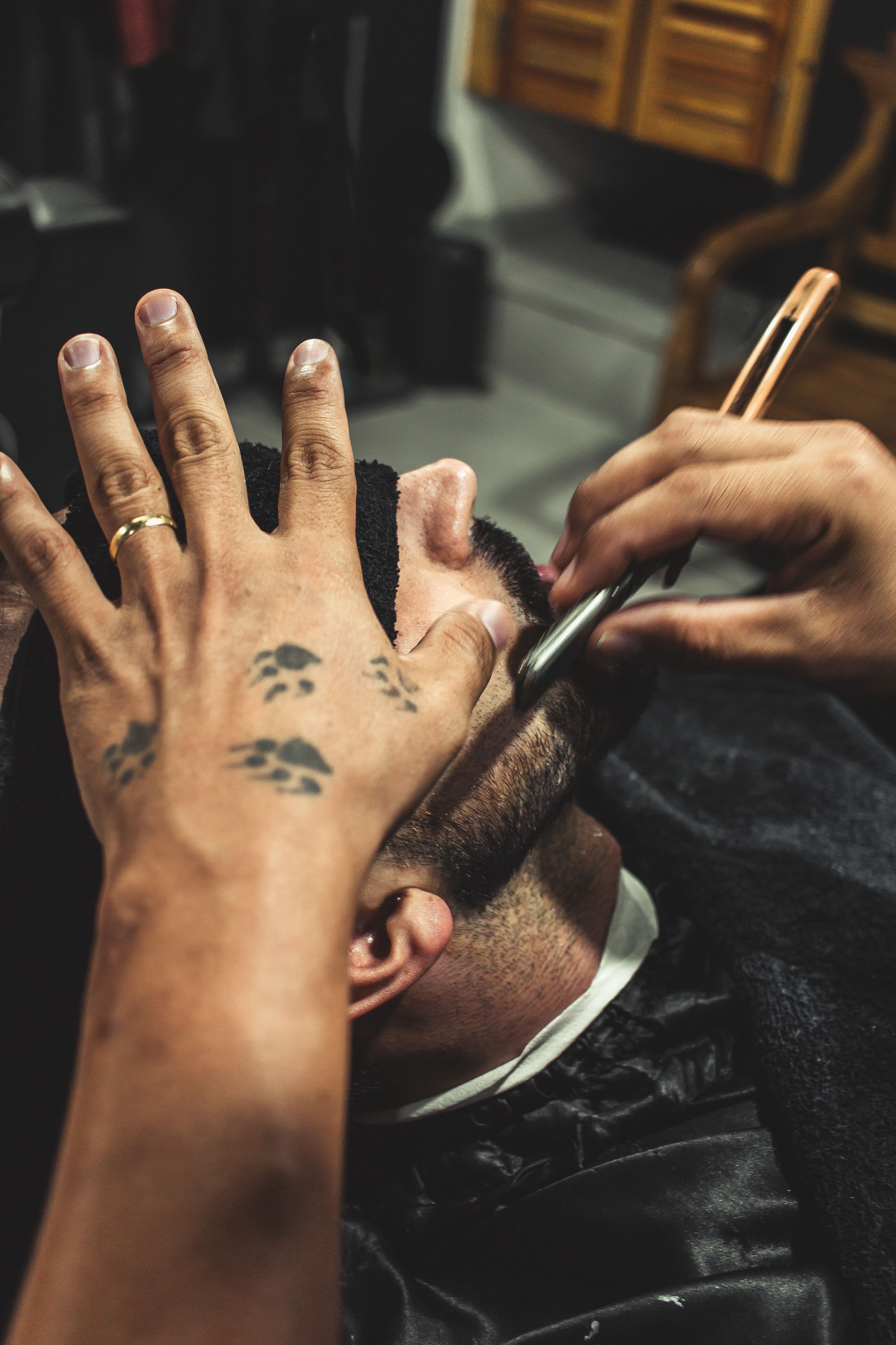 A barber with paws tattoos shaving a beard with razor