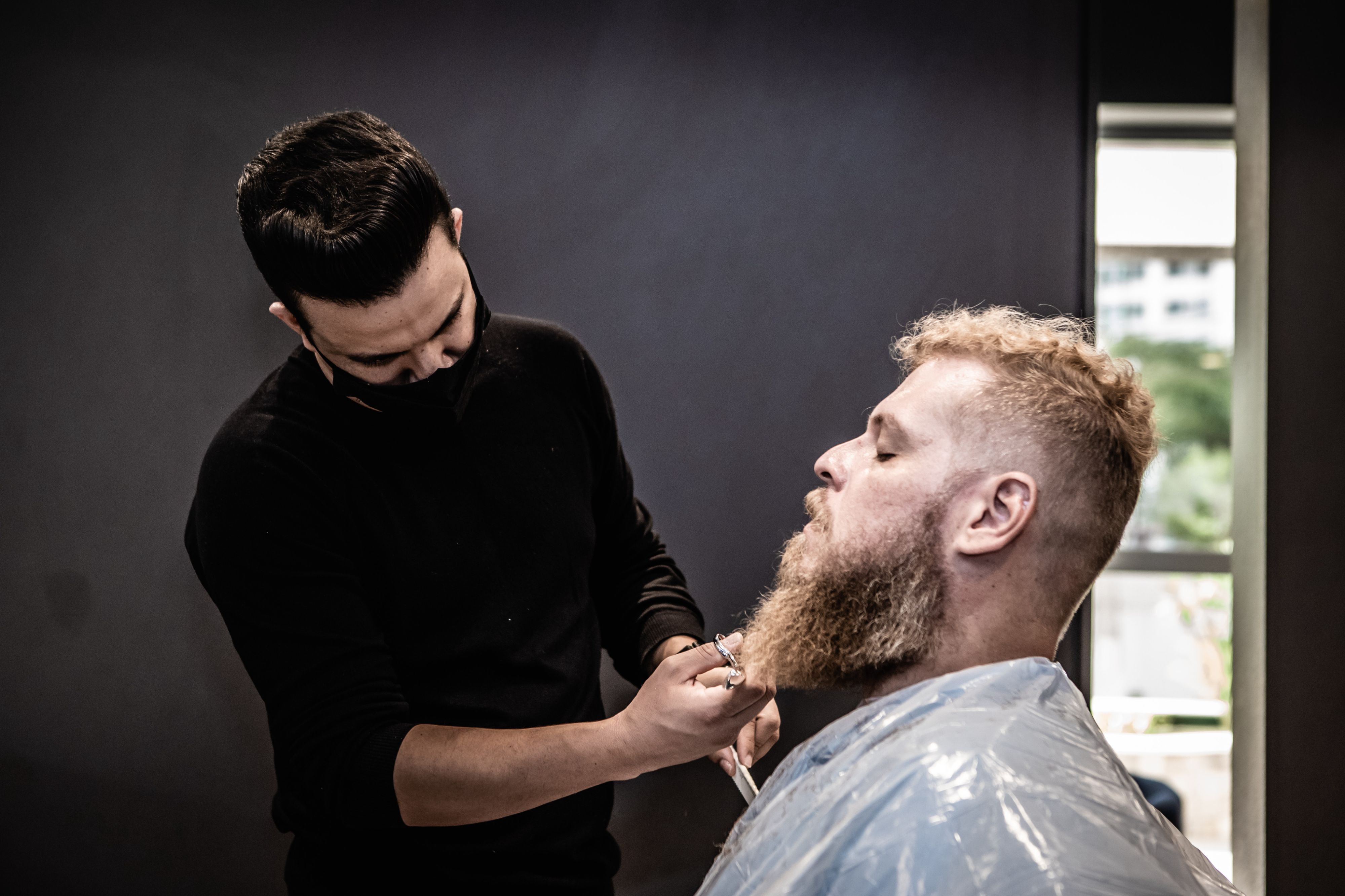 A barber with mask trimming the beard