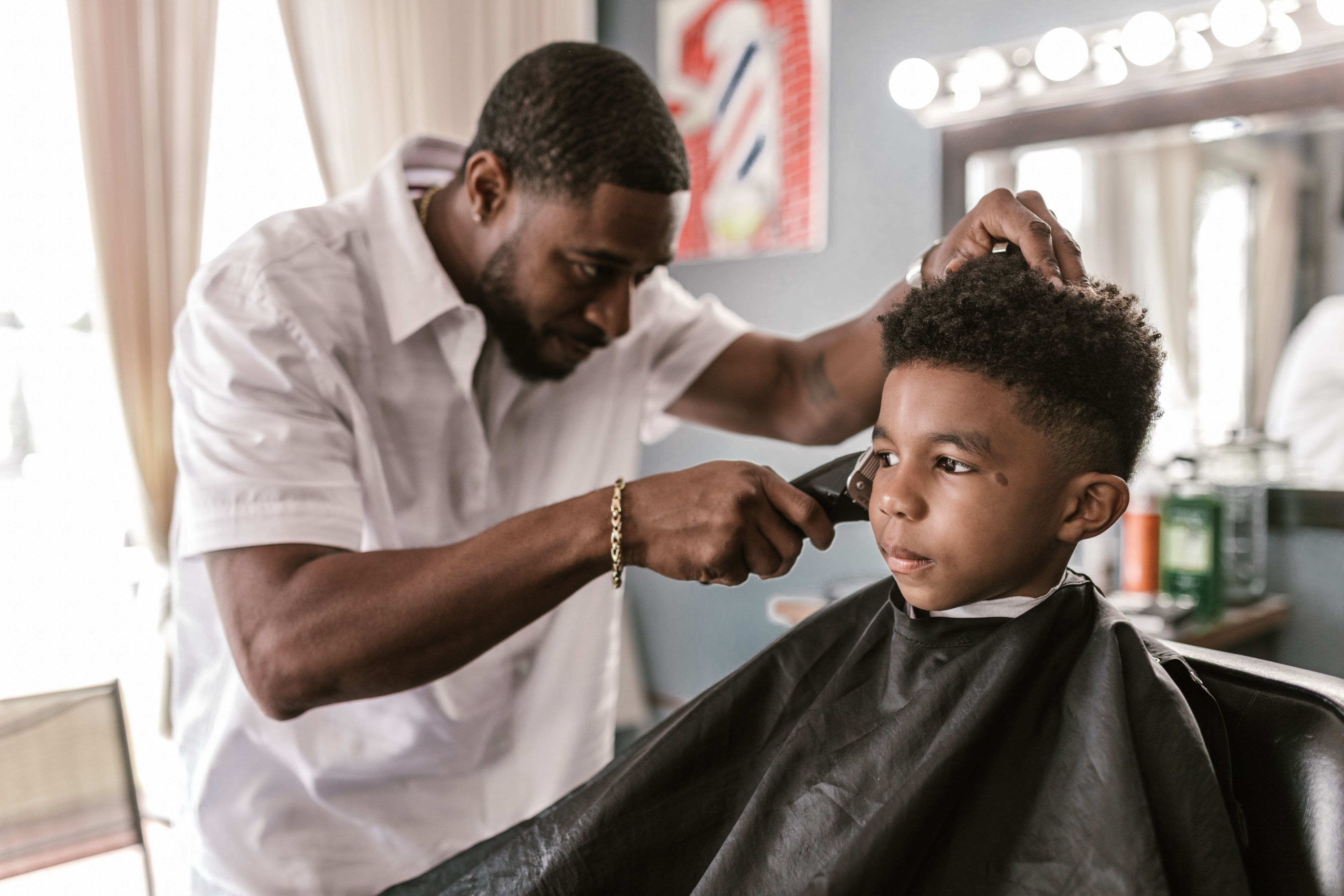 A black man with bracelet cutting a black little boys hair.